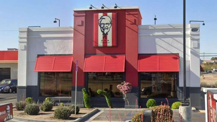KFC restaurant exterior with red columns, Colonel Sanders sign above the entrance, and large front windows.